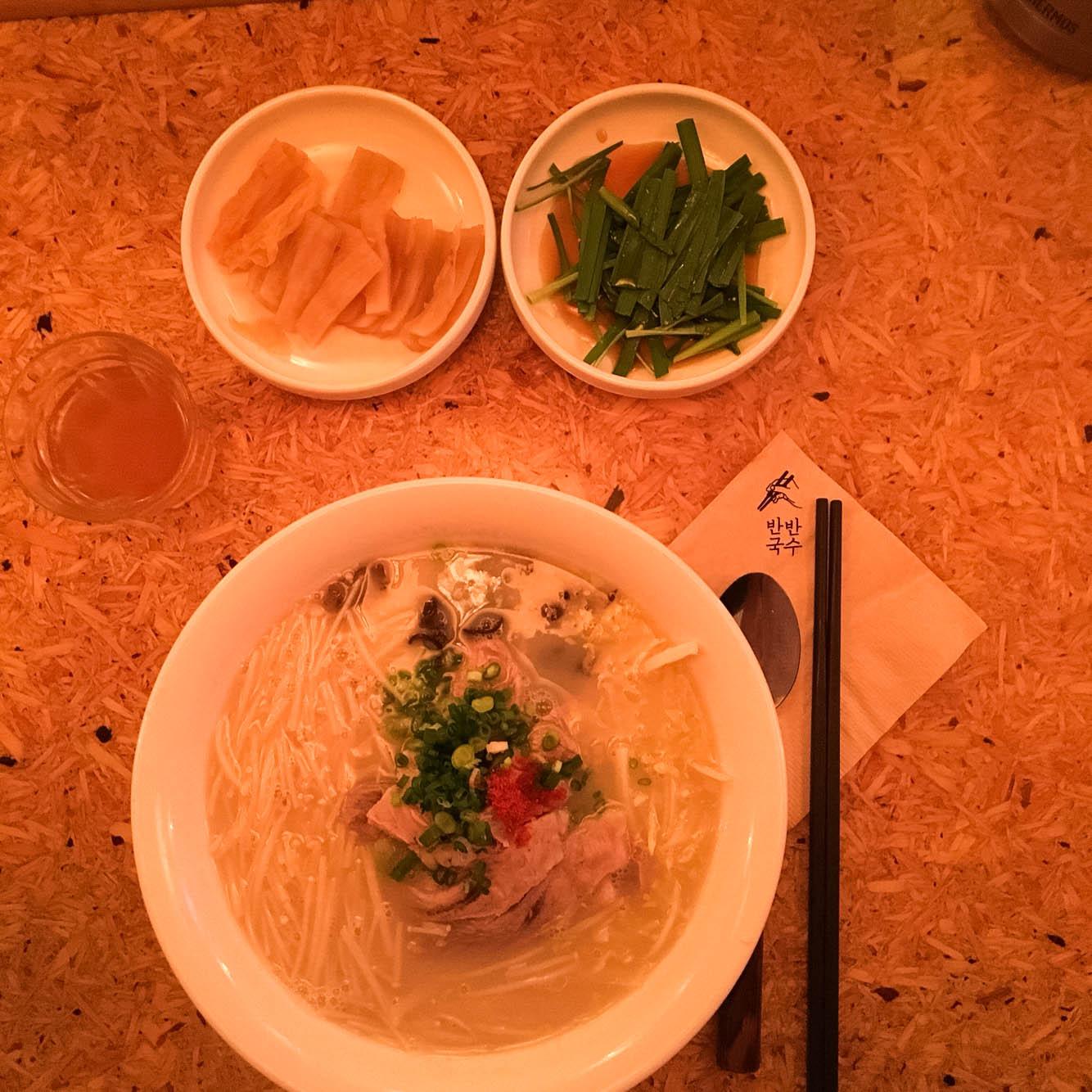bowl of half-and-half noodle soup, a popular staple food in Seoul, Korea. Tableware and ingredients shown in background.