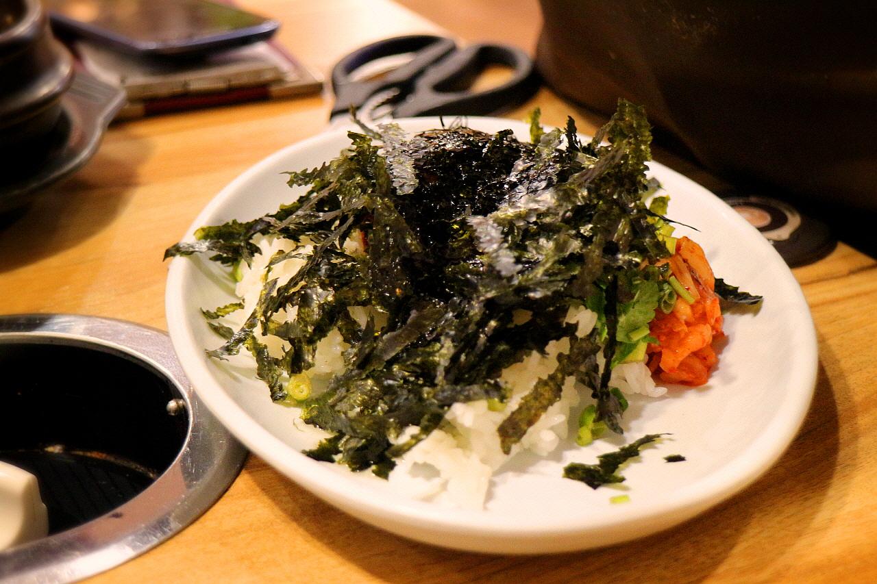 A plate of savory T-bone steak with leafy greens, accompanied by kitchen utensils, recipe ingredients and fine herbs.
