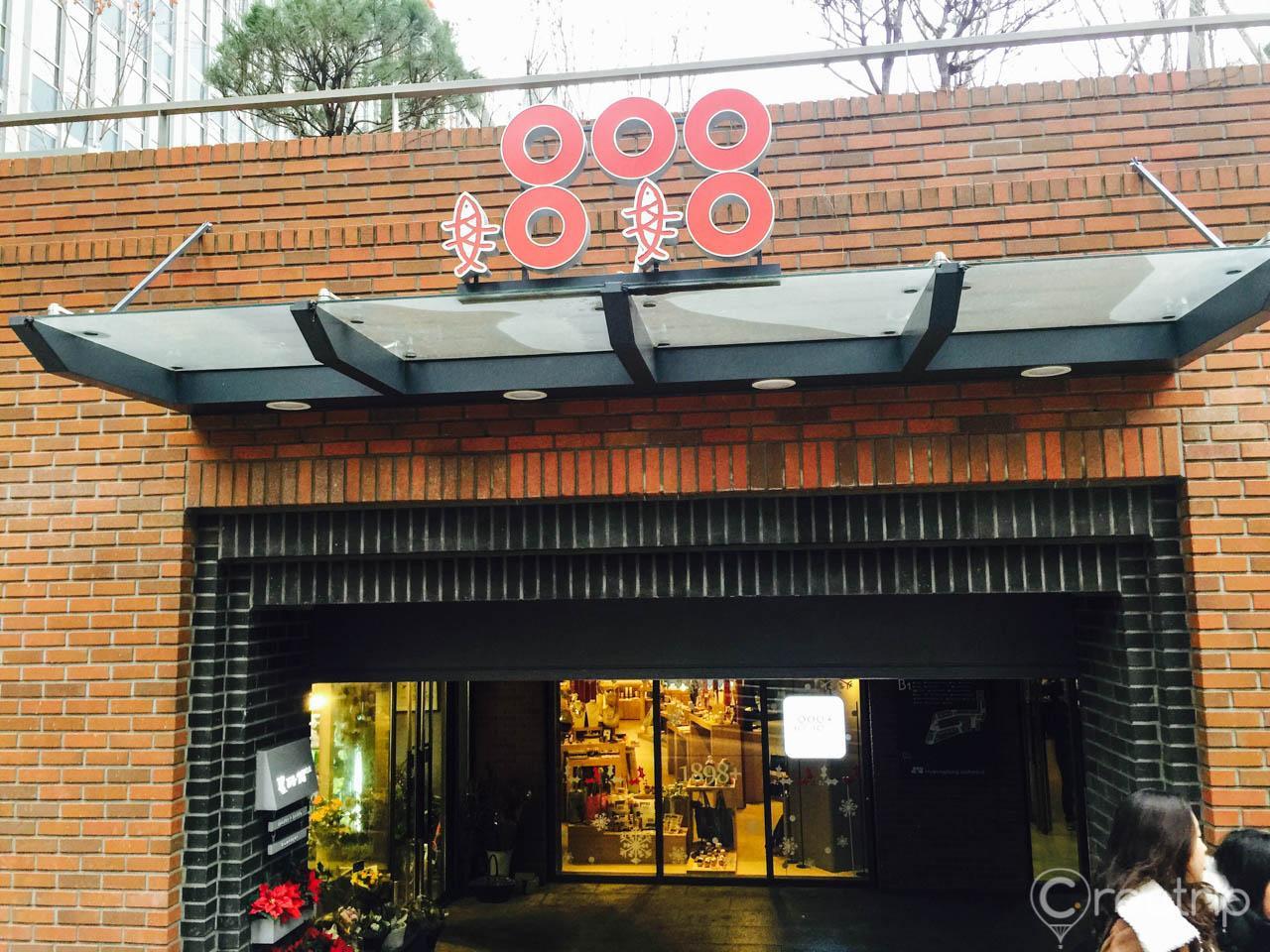 The 1898 Plus storefront in Seoul features a brick façade with a tire and wheel property, surrounded by trees.