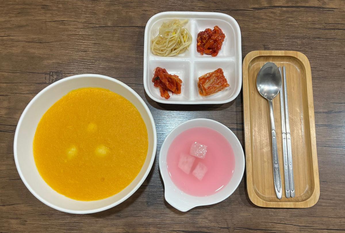 A Korean meal featuring traditional dishes including pumpkin porridge and papaya juice.