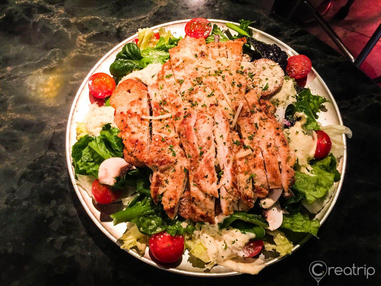 Jacoby Burger topped with broccoli and leafy greens on a festive table with dishes and ingredients.