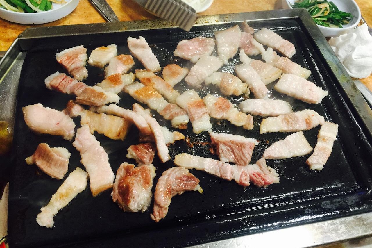 A platter of 삼겹살 (pork belly) at 서문돌판생삼겹살 restaurant. Other food and drink items on a Korean outdoor grill.