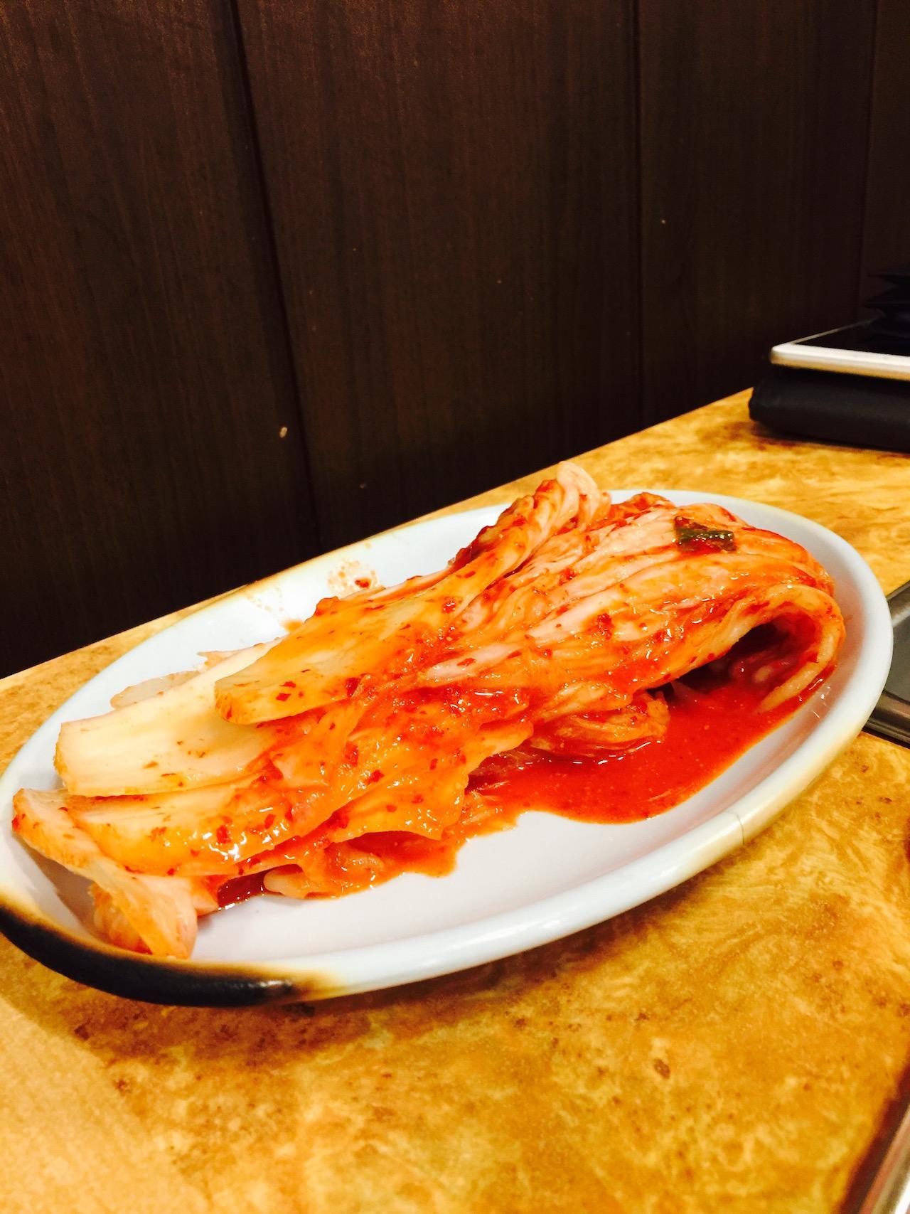 Plateful of 서문돌판생삼겹살, topped with tangy tomato sauce and spicy 김치, a classic Korean food favorite.