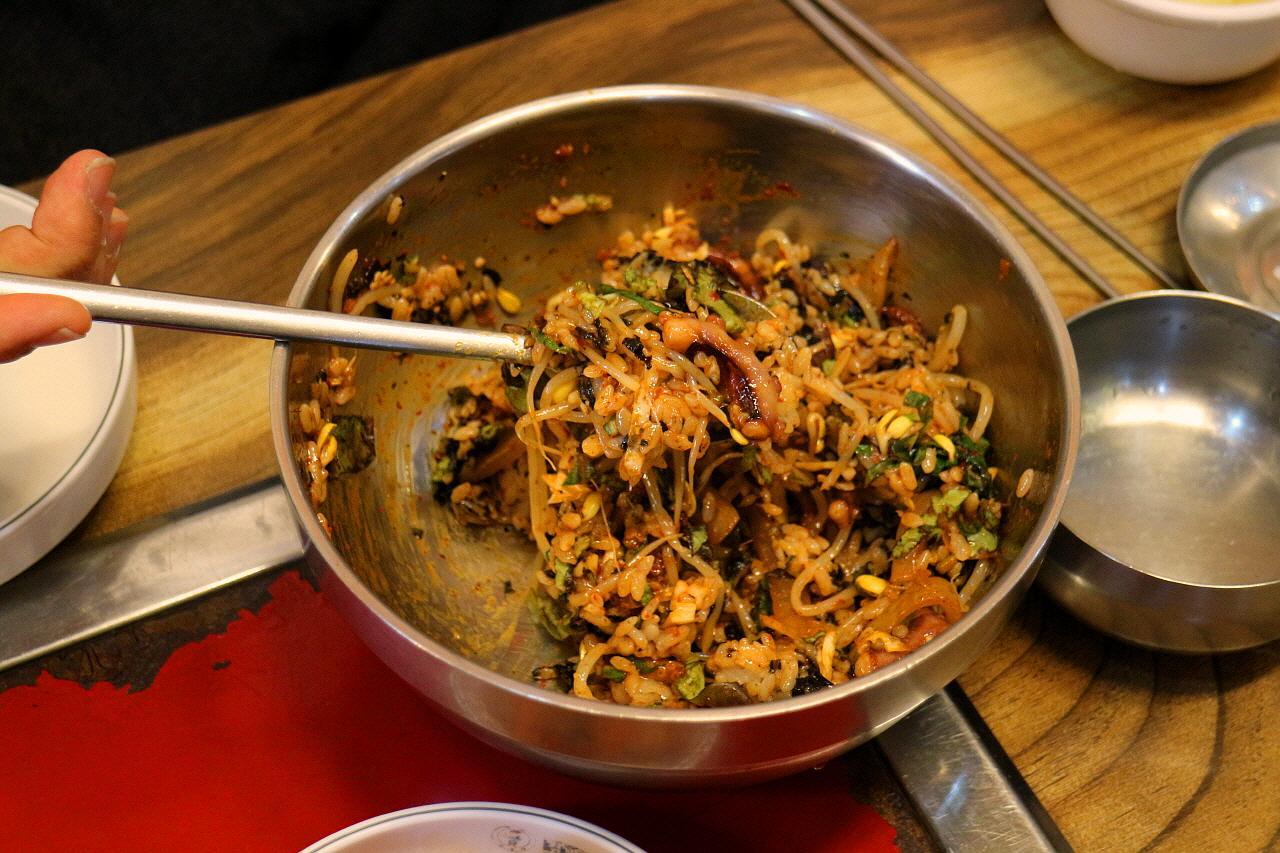 A bowl of 굴국밥, a Korean staple food made with a mixture of ingredients and produce, served on tableware in a traditional kitchen setting.