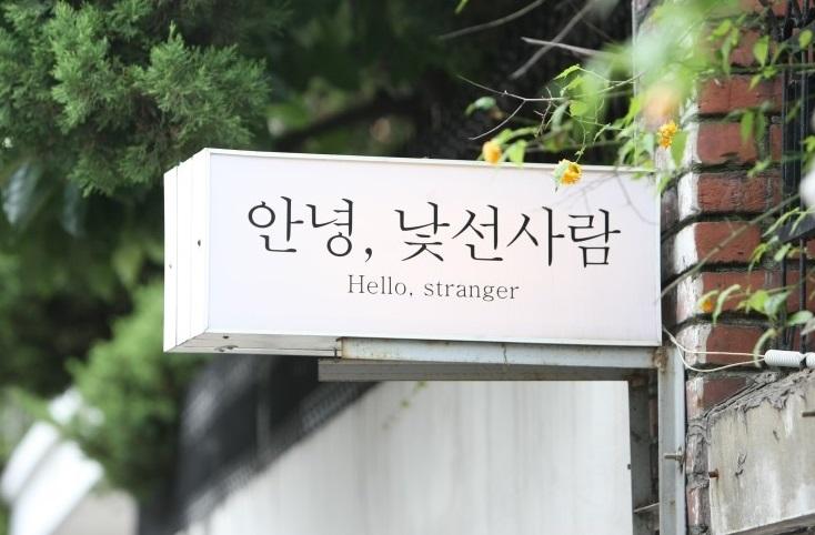 Signage outside <Annyeong, Stranger> restaurant/cafe with plant, wood and grass elements in Seoul, Korea.
