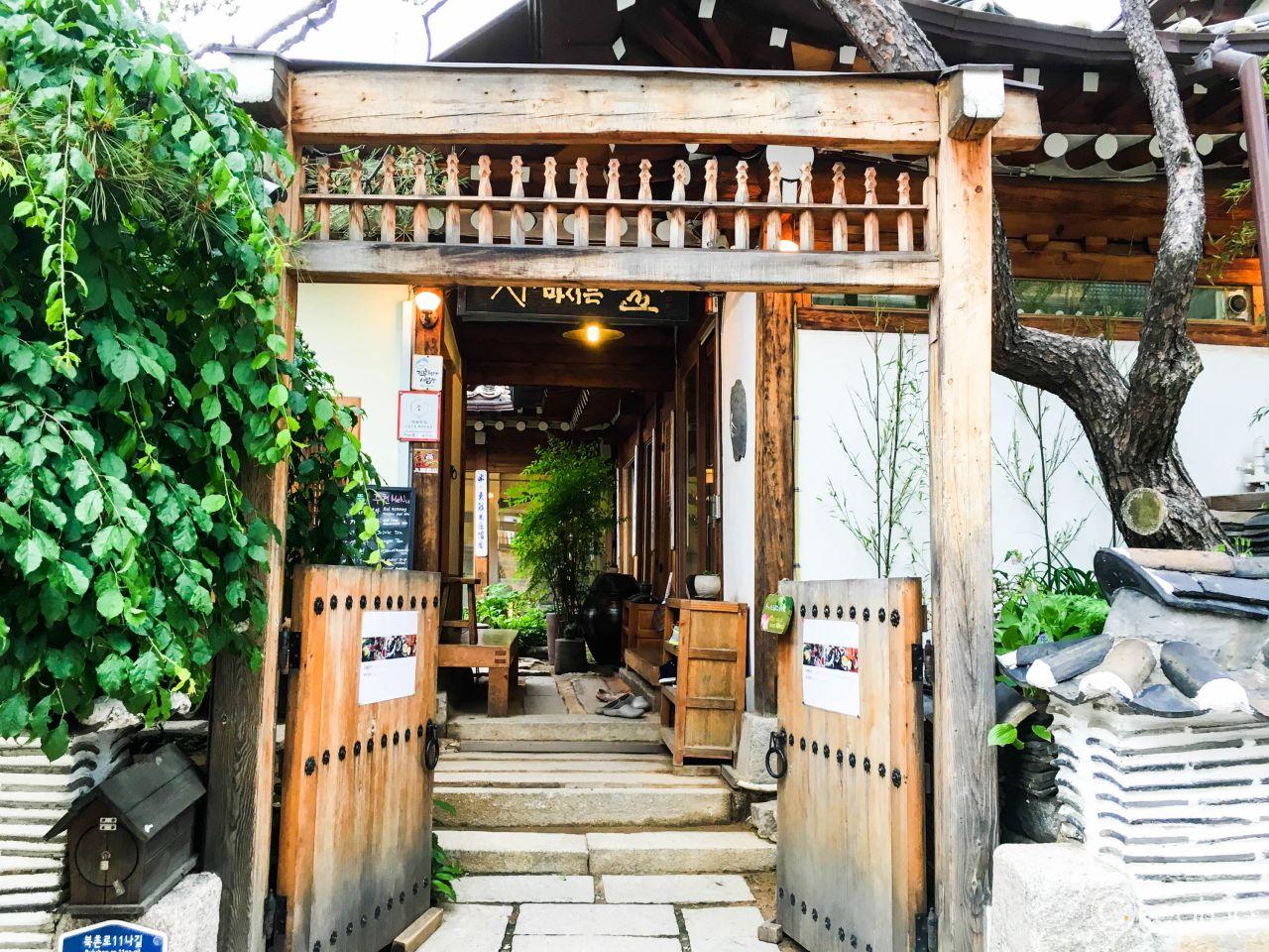 Outdoor seating area surrounded by lush greenery and wood building with open door in Korea.