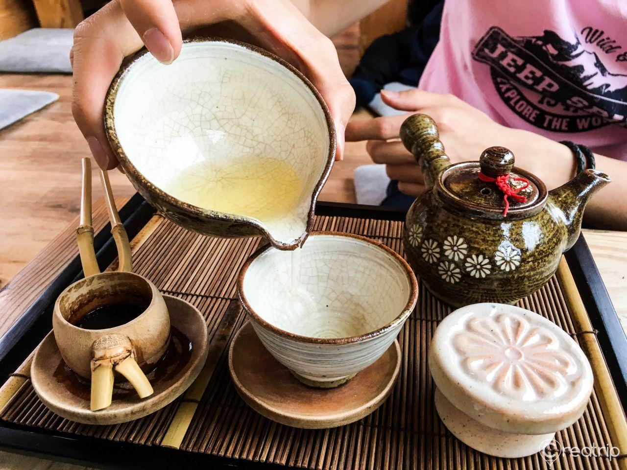 A woman enjoying a cup of tea in a Korean courtyard with tableware and ingredients.