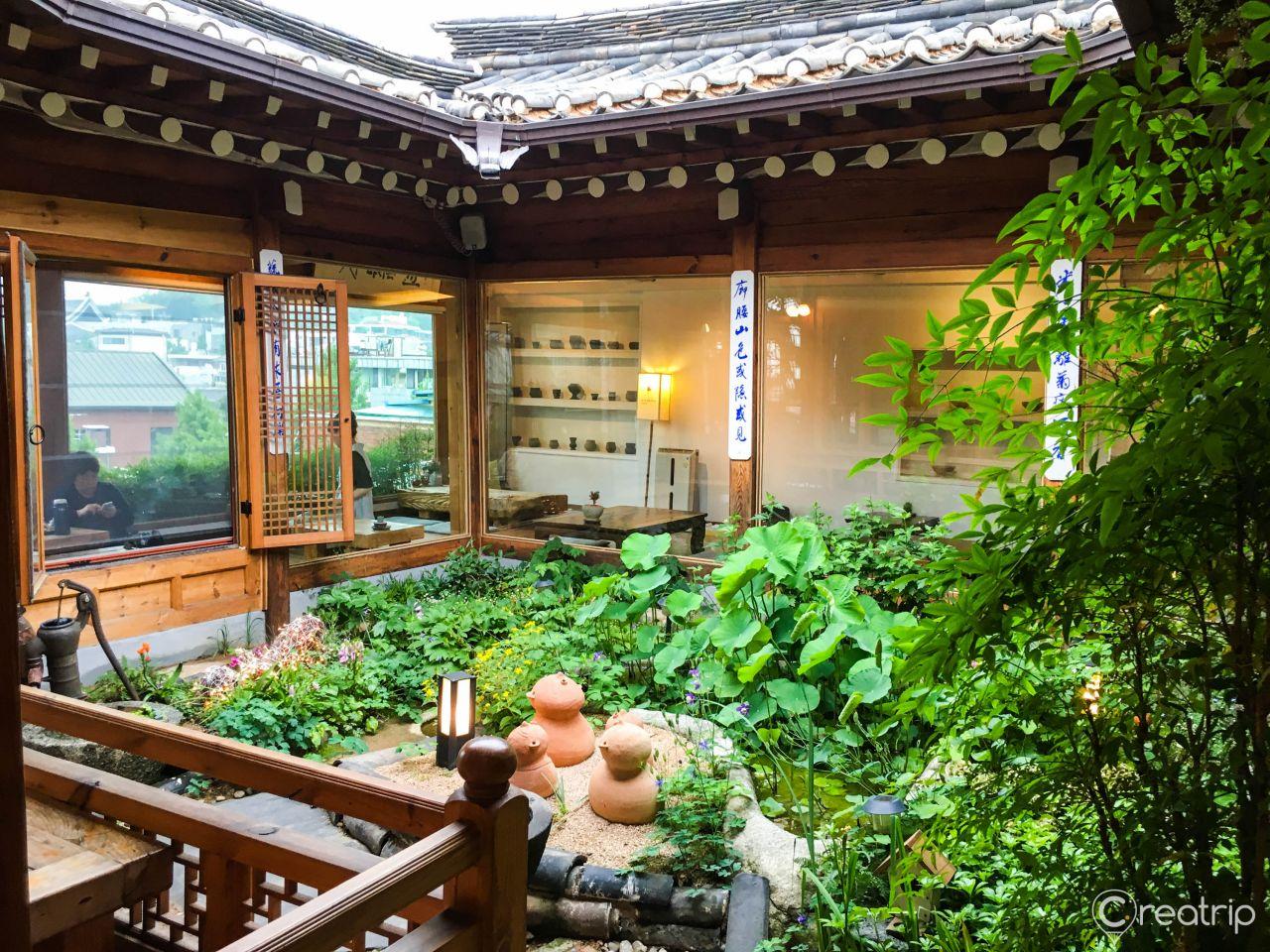 A tranquil garden scene with a cottage, shade trees, and lush green grass.