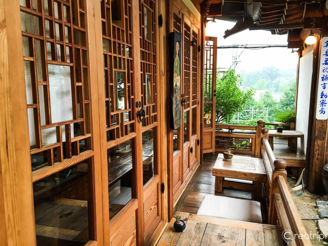 Interior of a wooden room with plants and trees, featuring hardwood flooring and wooden beams.