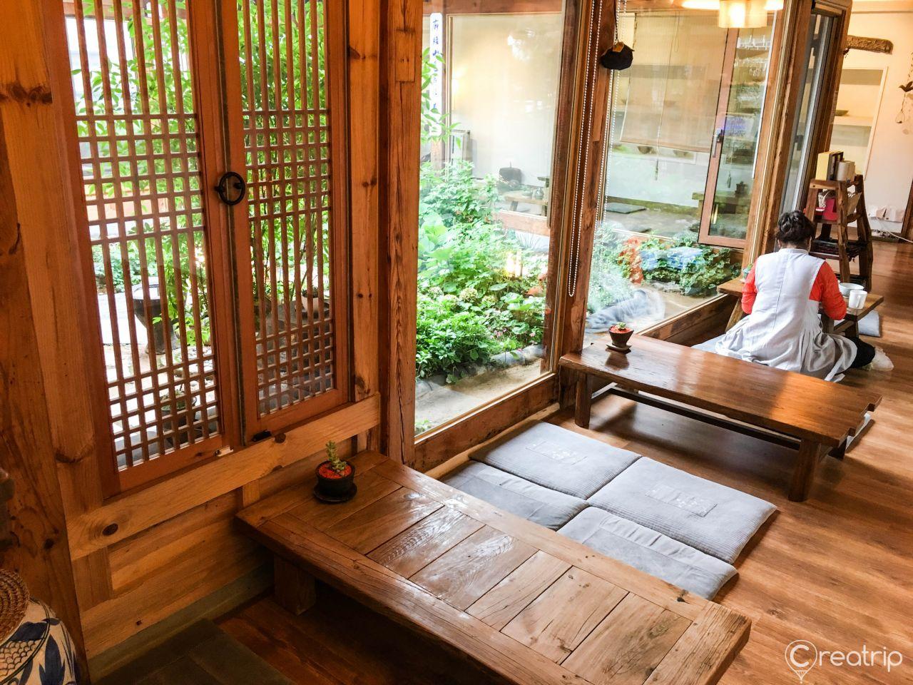 Interior view of a room in Korea with wooden flooring, table, plants and a window with a view.