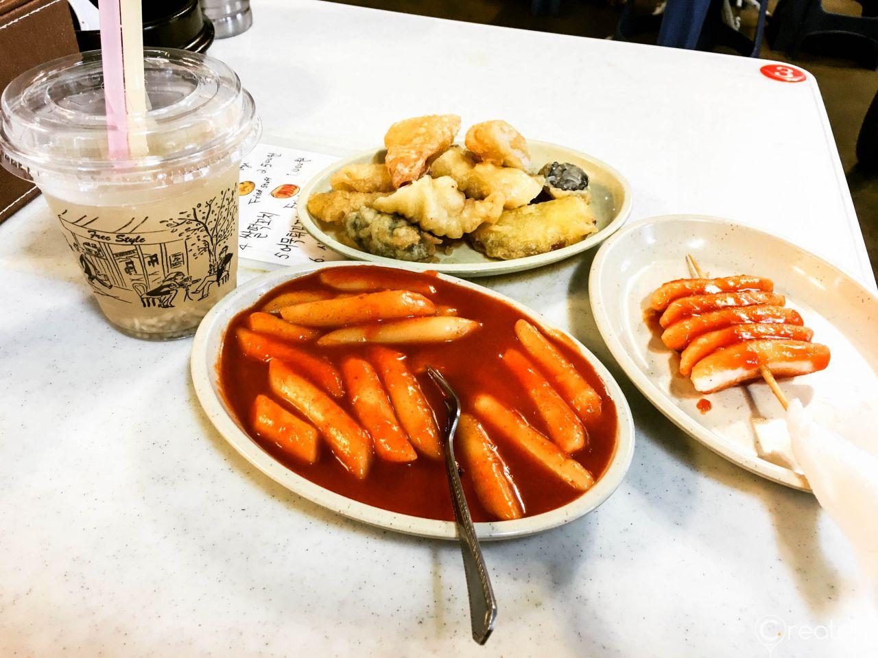 A plate of delicious Korean street food, including spicy ddeokbokki (rice cakes), falukorv, and rice, served on traditional tableware.