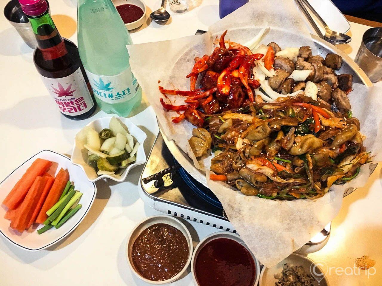 A delicious spread of Korean cuisine featuring grilled pork intestines, plates of pickled vegetables, and soy sauce bottles on a wooden table.