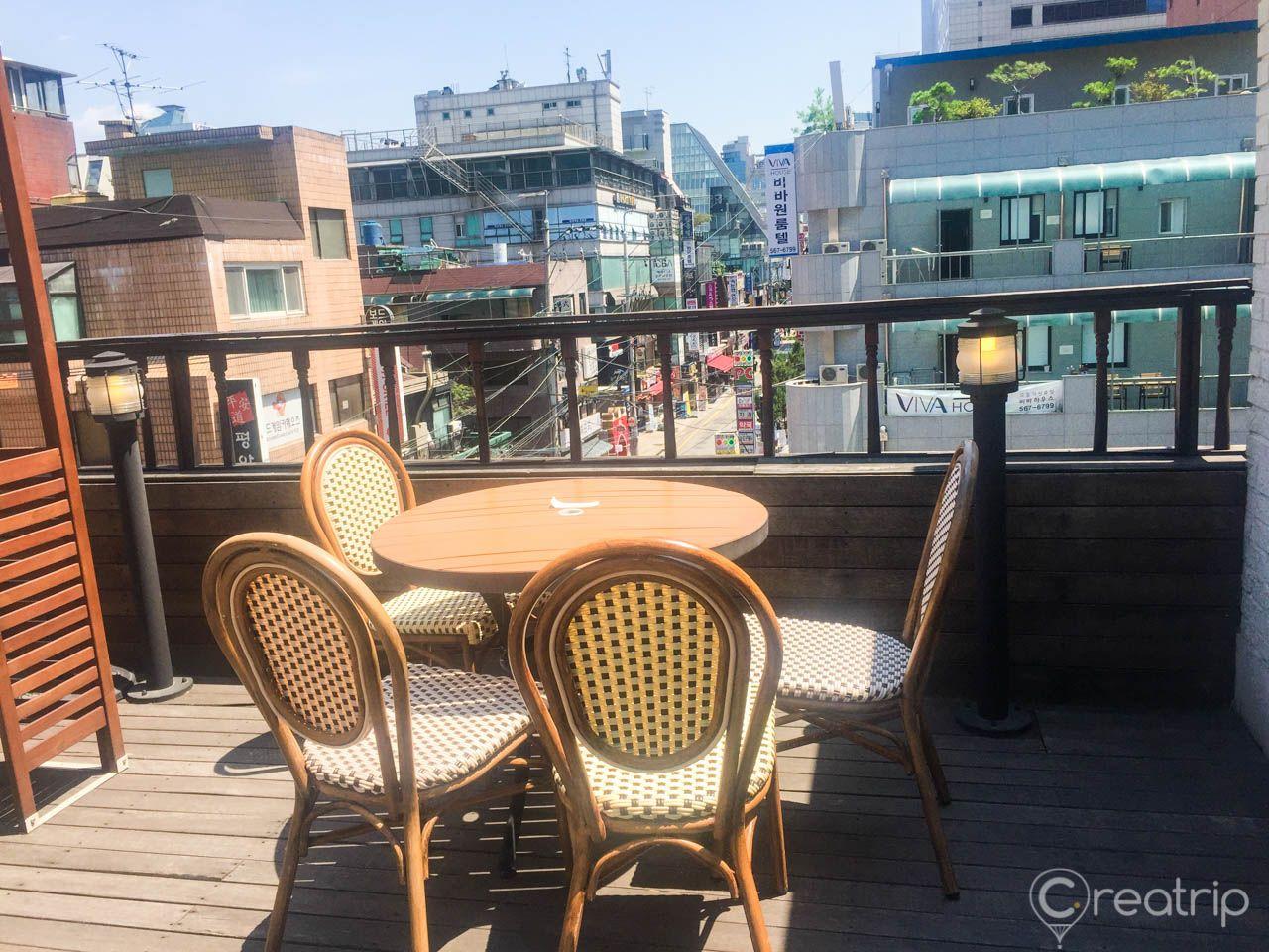 Outdoor rooftop café with wooden furniture at Chloris Yeoksam GFC branch in Seoul's urban condominium building.