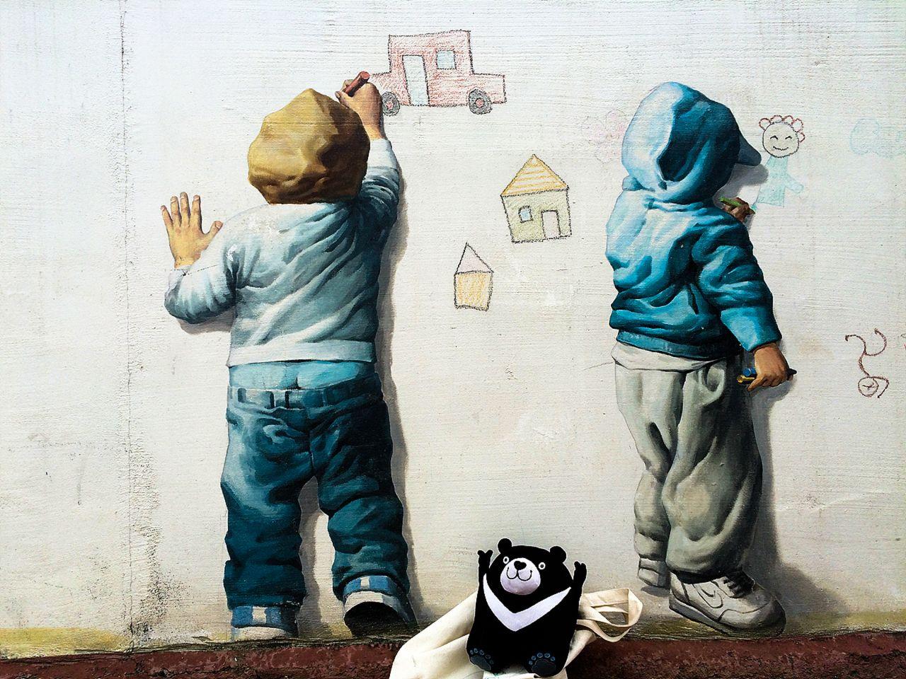 white graffiti art on a cool grey wall at 가덕도 정거마을 with standing textile and text in bold font.