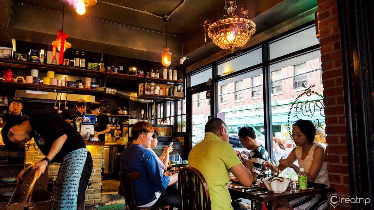 Seafood pasta dish on a table with chairs and barware in a Korean drinking establishment.