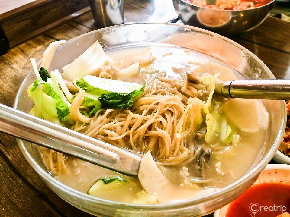 photo of a traditional Korean meal featuring Pyeongyang-style cold noodles, accompanied by various types of tableware and ingredients for making the soup.