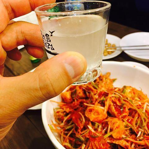 A table setting with various traditional Korean dishes including crispy pan-fried golbaengi (whelk) and Chinese-style noodles, accompanied by soju and soft drinks.