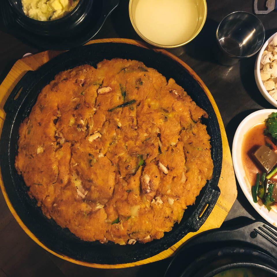 korean-style platter of savory pancakes and various side dishes on a table set with dishware and tableware in a bustling food alley