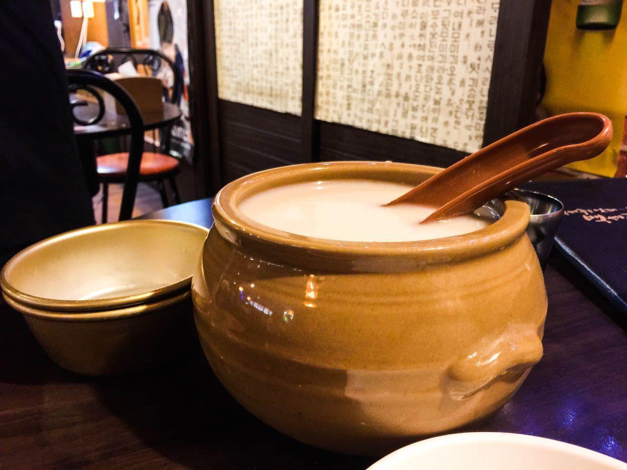 korean-style dish of pajeon, a savory pancake, served with makgeolli and various dishware and ingredients on a wooden table.