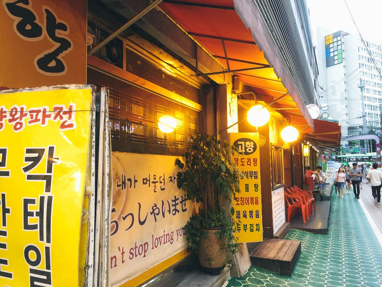 yellow flowers in pots adorn the facade of a building on a bustling city street in Korea's 회기 파전골목.