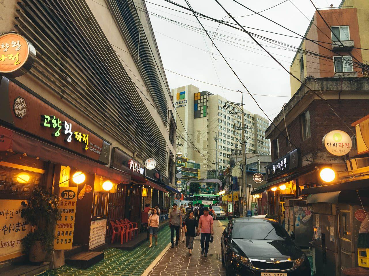 a car parked in front of a building in the vibrant district of 회기 파전골목 with a tire in the foreground.
