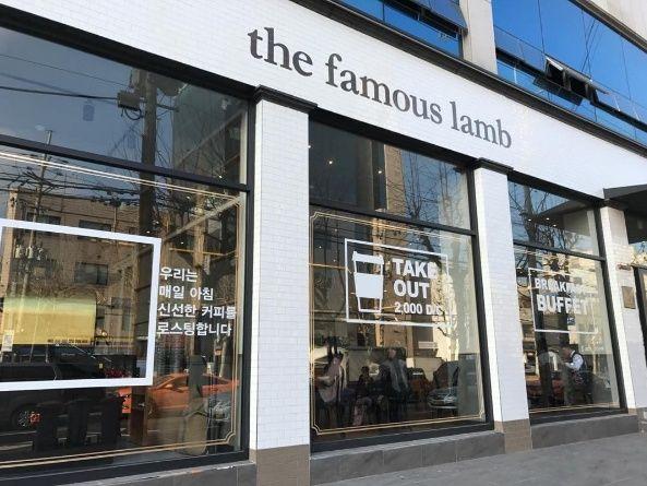 Exterior of a mixed-use building with a prominent '더페이머스램' sign, showcasing a bakery display case and coffee shop in a modern glass facade.