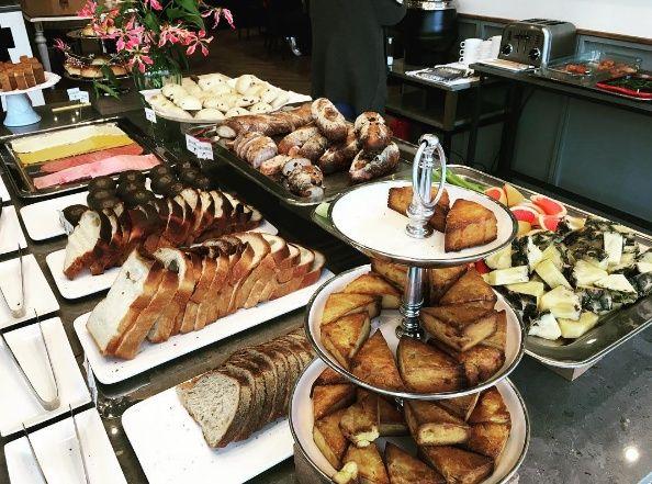 A buffet table displaying various dishes including The Paemir's lamb, bread, coffee, and tableware in a Korean setting.