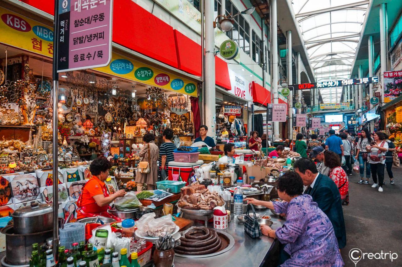 A bustling market in Korea's city center featuring a temple, street vendors, and shoppers.