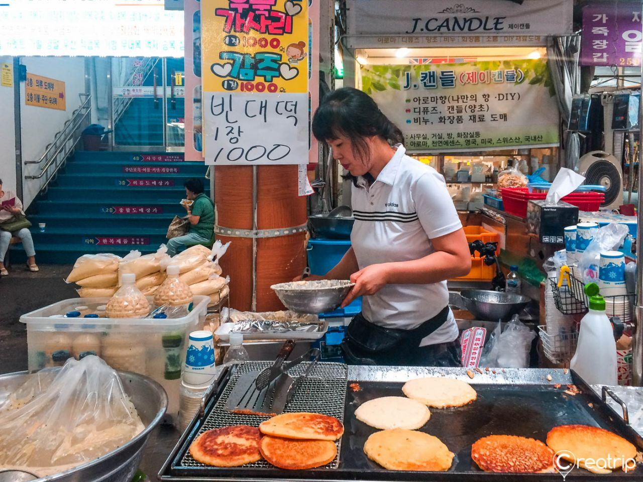 Colorful cuisine dishes and fast food for sale at the bustling 서문시장 market in a Korean city.