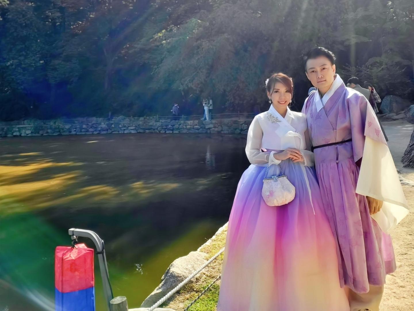 Group of happy people in traditional Korean hanboks and formal wear posing by the lake surrounded by trees in Gyeongbokgung, Seoul | Hanbok rental shop.