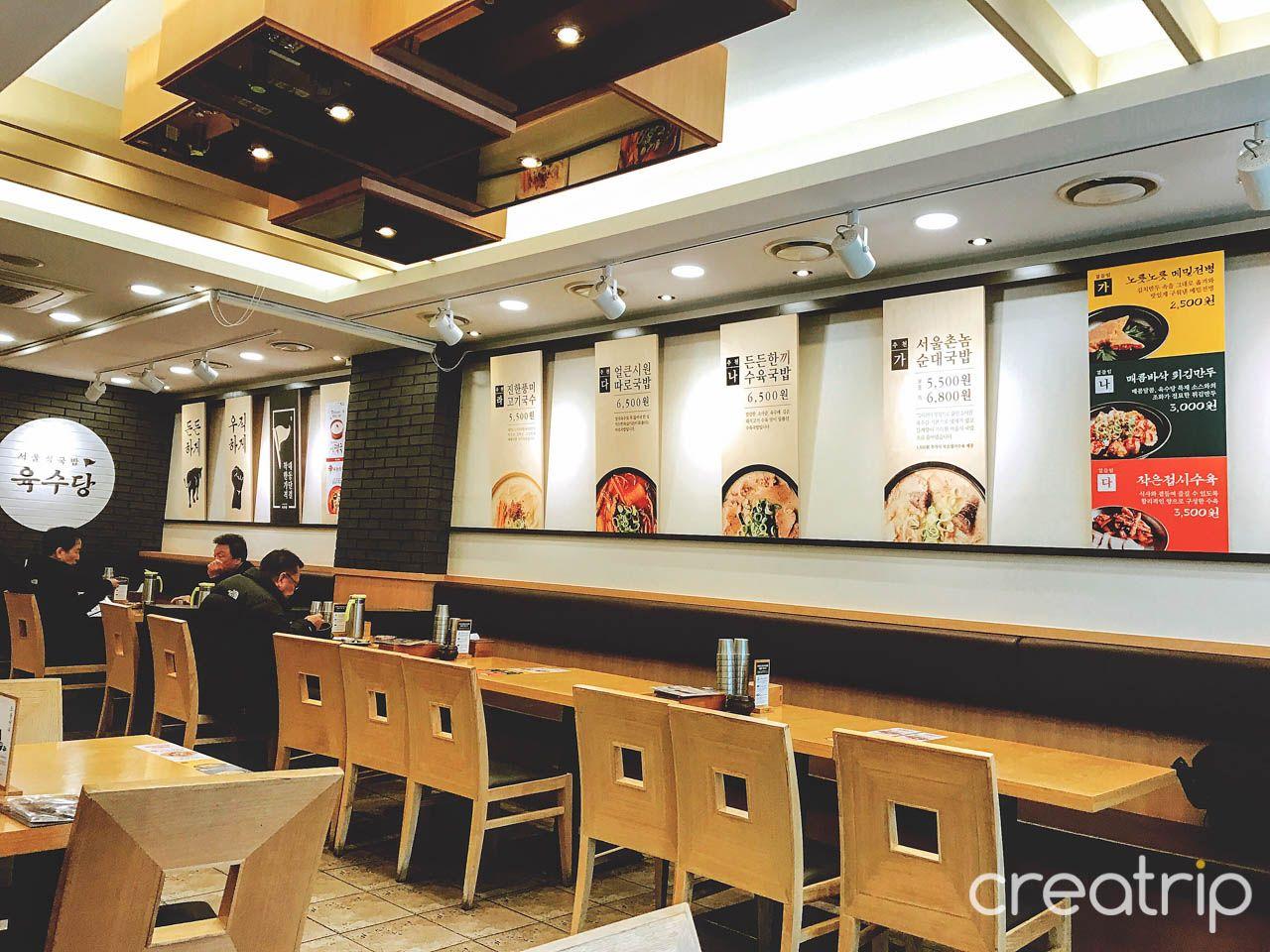 Interior of 육수당 충무로점 restaurant with modern architecture, stylish lighting, tables, chairs, and event desk.