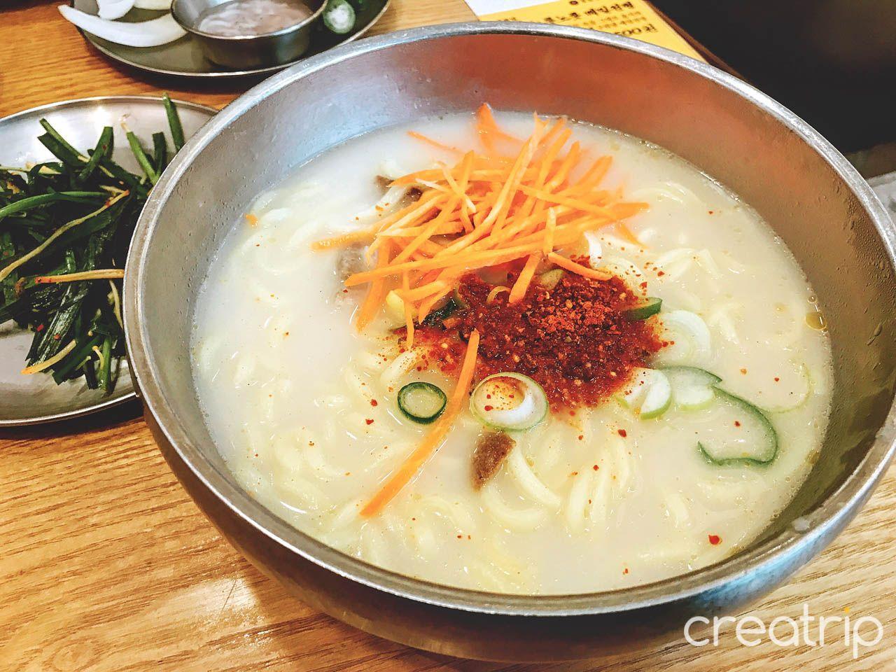 A bowl of hearty 수육 국밥 at 육수당 충무로점 with noodle, soup, and ingredients on tableware.