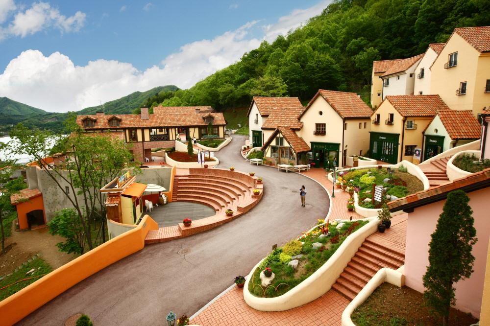 A scenic view of a French town in Korea with Italian village vibes. Clouds and trees frame urban design of buildings and properties with classic windows.