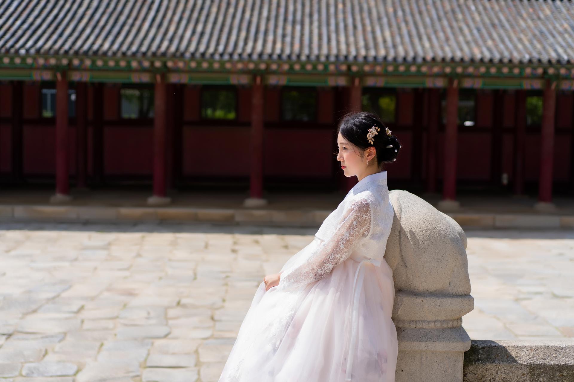 A woman in traditional Korean hanbok clothing standing outside a temple rental shop, adorned with embellishments and sweeping sleeves.