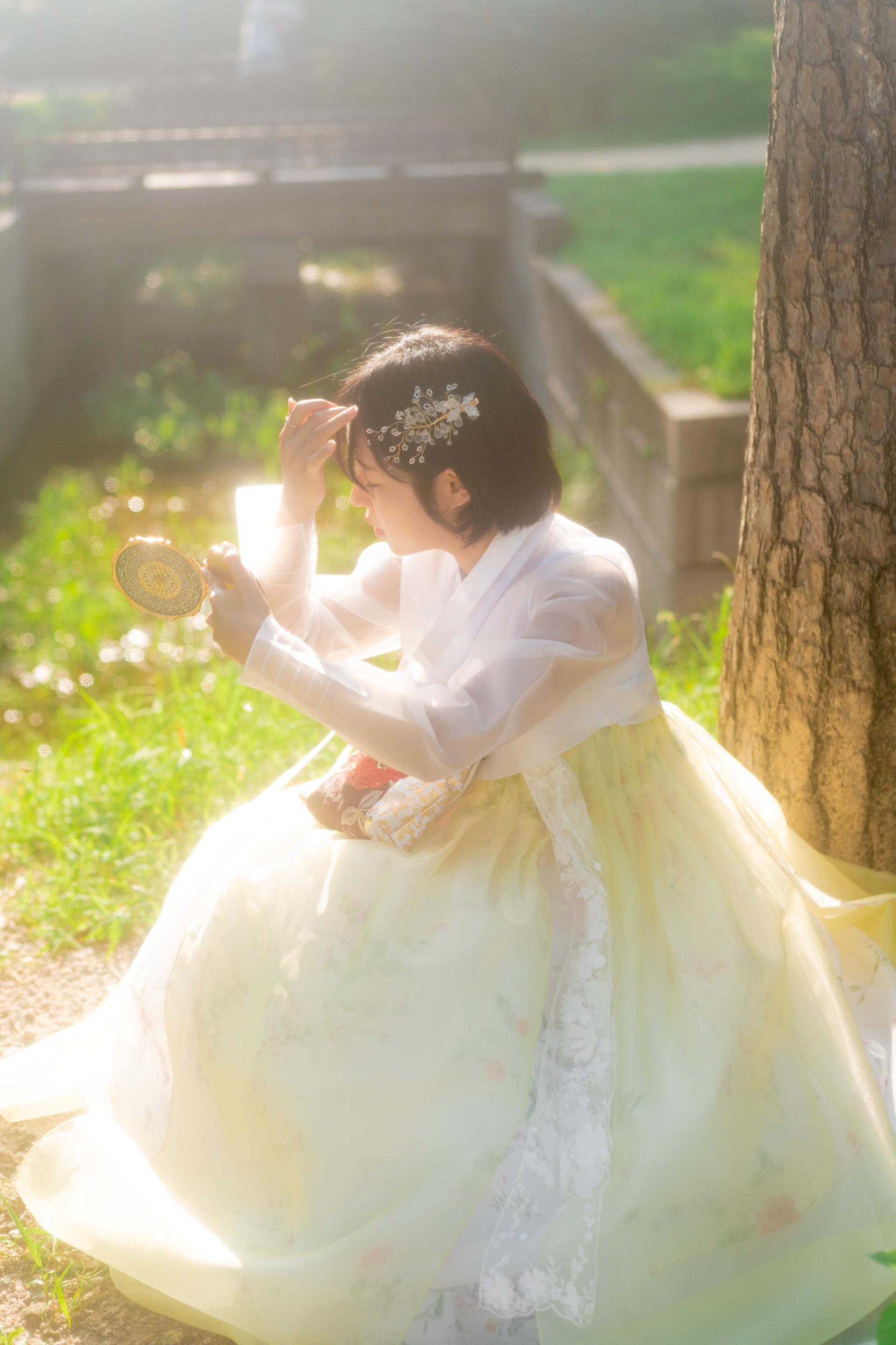 Happy people enjoy leisure time in nature, wearing hanbok and dresses, while surrounded by greenery and sunlight.