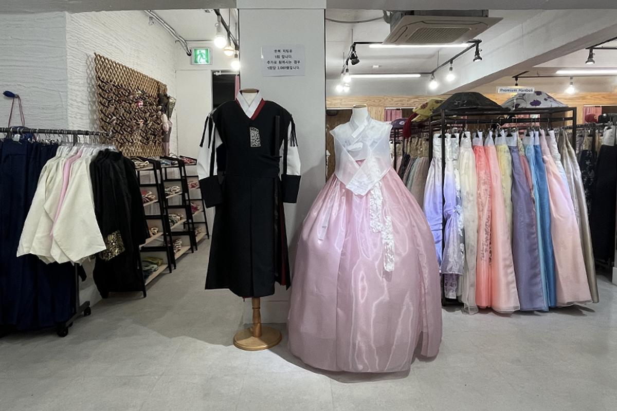 traditional Korean hanbok stands in a boutique filled with one-piece garments, clothes hangers, and retail items. Gyeongbokgung hanbok rental shop provides options for formal wear and fashion enthusiasts.