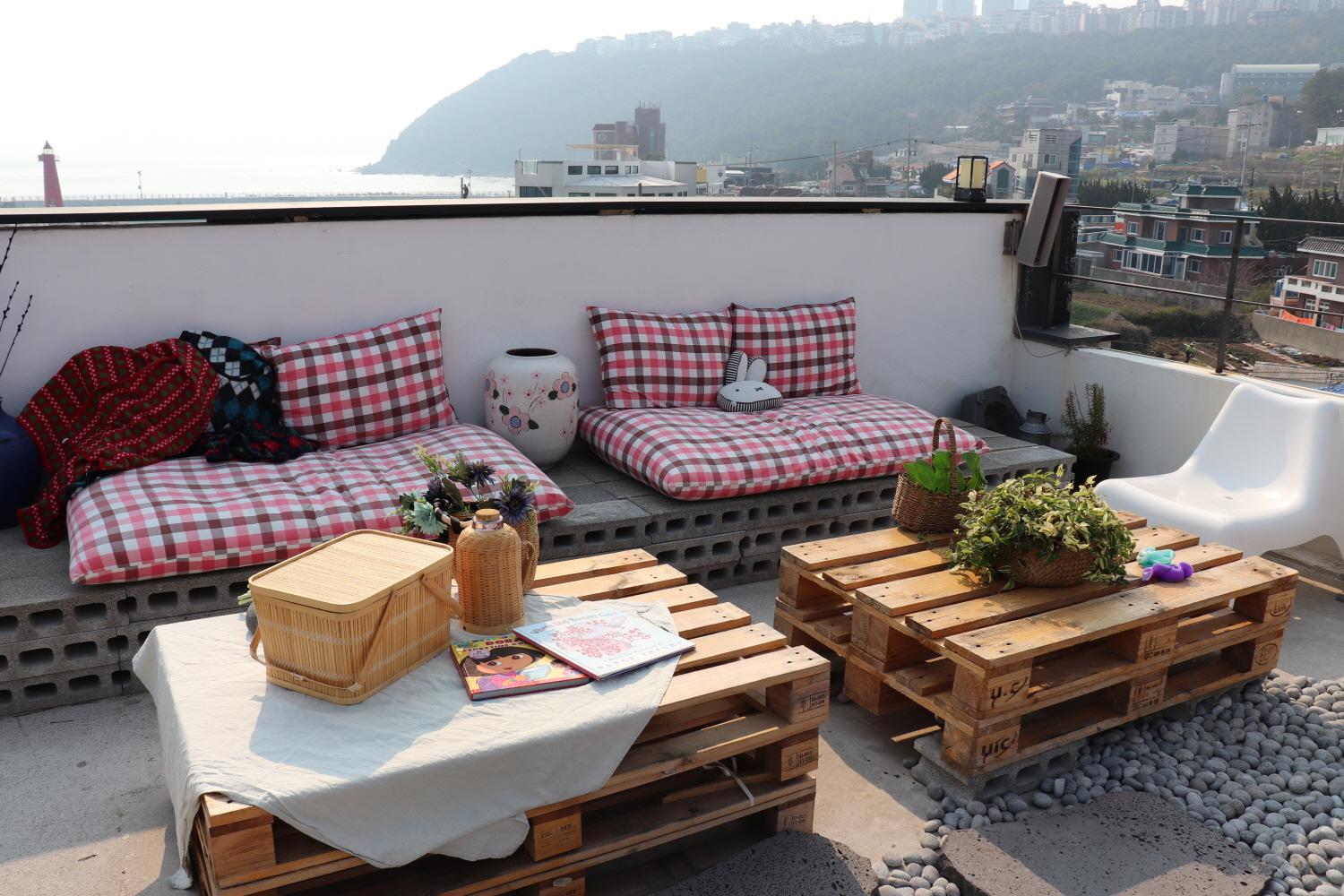 rooftop cafe with stylish furniture, including a couch, table and outdoor seating. Plants and flowers accent the modern interior design.