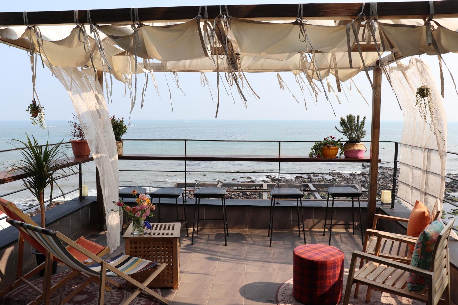 rooftop café with Water view, Skyline and Outdoor Furniture including Wooden Tables & Chairs, Plants, and Shades.