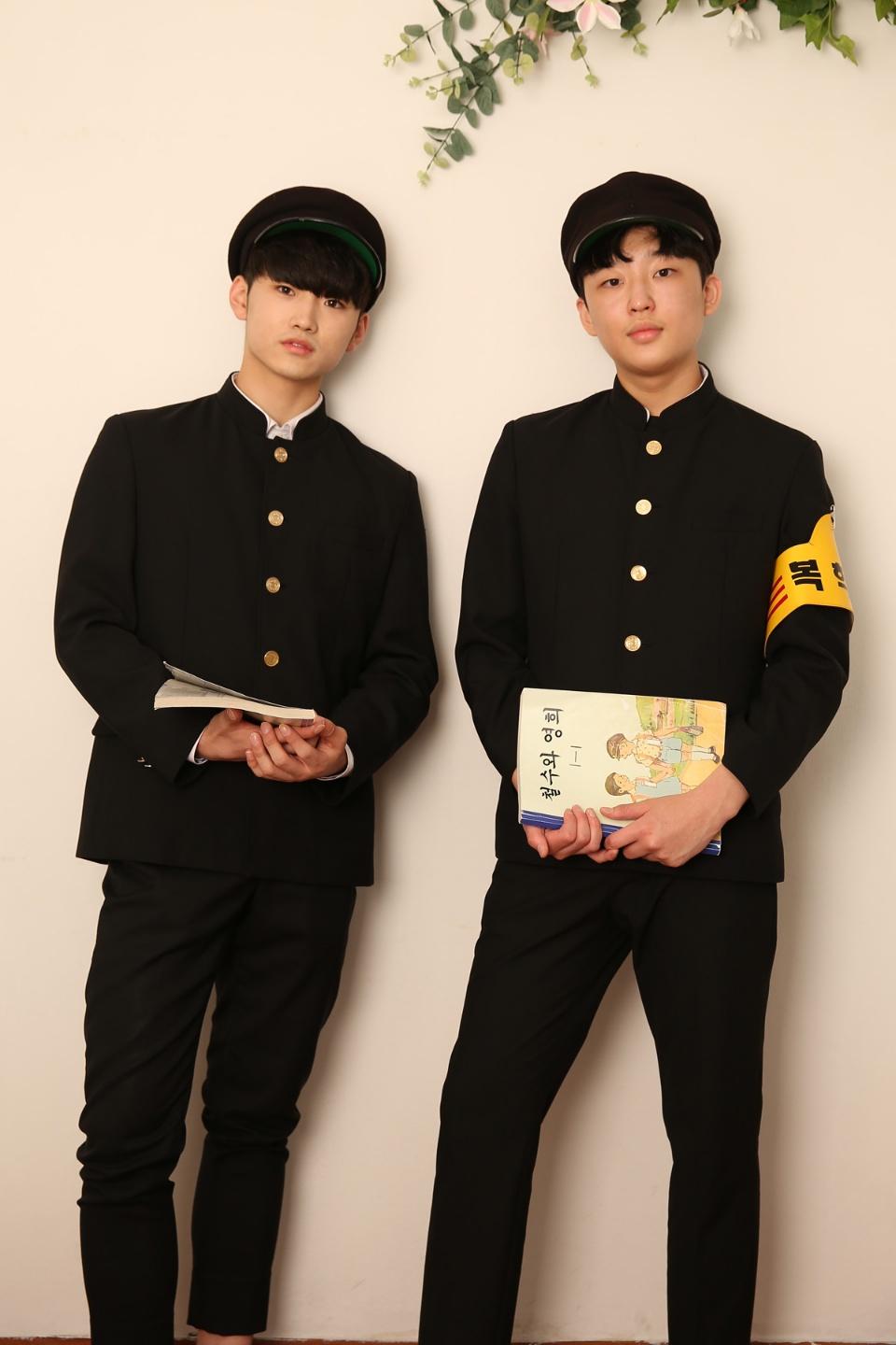 Two people. in school uniforms stand side by side with gestures.