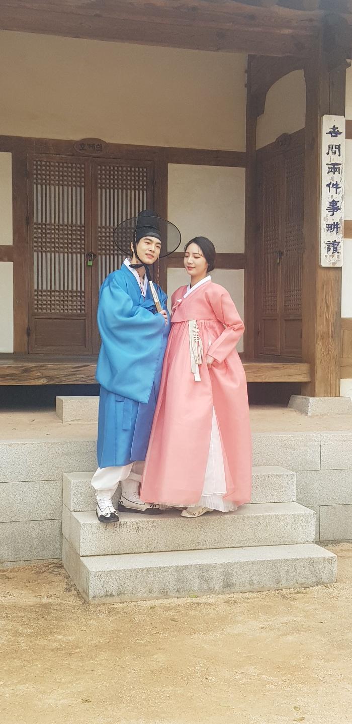 A happy Korean couple in traditional Hanbok formal wear outside a temple in Busan, smiling and having fun at an event.