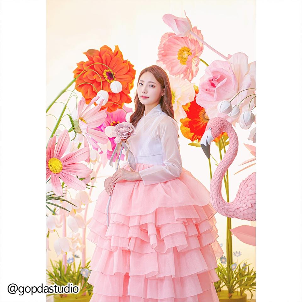 A model wearing a pink hanbok dress with floral accents stands in a Korean Hanbok rental shop in Busan.