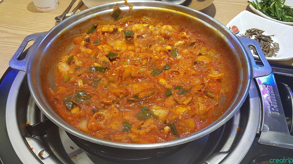 a photo of a dish called 낙지볶음 at 개미집 홍대점 restaurant in Korea. Contains ingredients such as meat, produce, and curry sauce in a karahi.