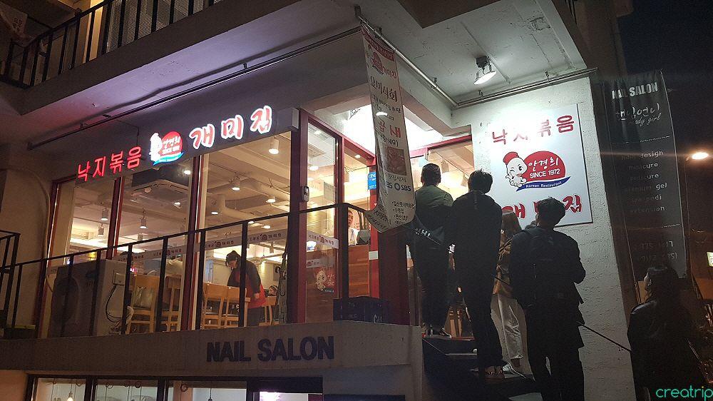 Exterior of 낙지볶음 개미집 홍대점, a retail building in Seoul with glass facade and advertising, shopping and event signs.