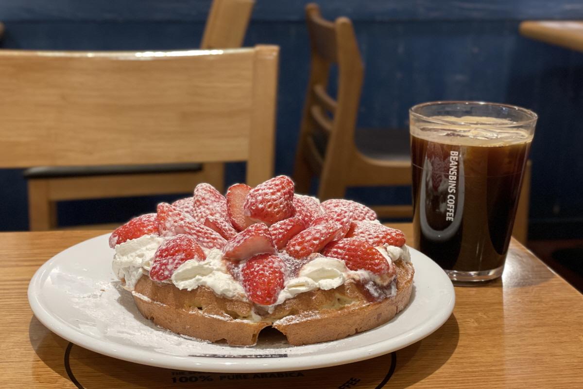A table at Beansbins Myeongdong, a dessert cafe in Seoul, featuring cake, strawberries, and drinkware.