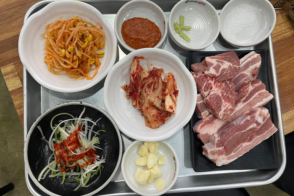 Plates of pork dishes on a table at 엉터리생고기 명동점, featuring 무한리필, with ingredients and tableware visible.