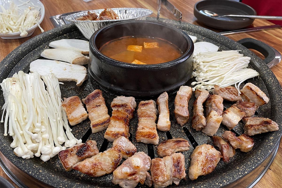 Delicious samgyeopsal dish with tableware and cooking ingredients on gas stove at 엉터리생고기 명동점.