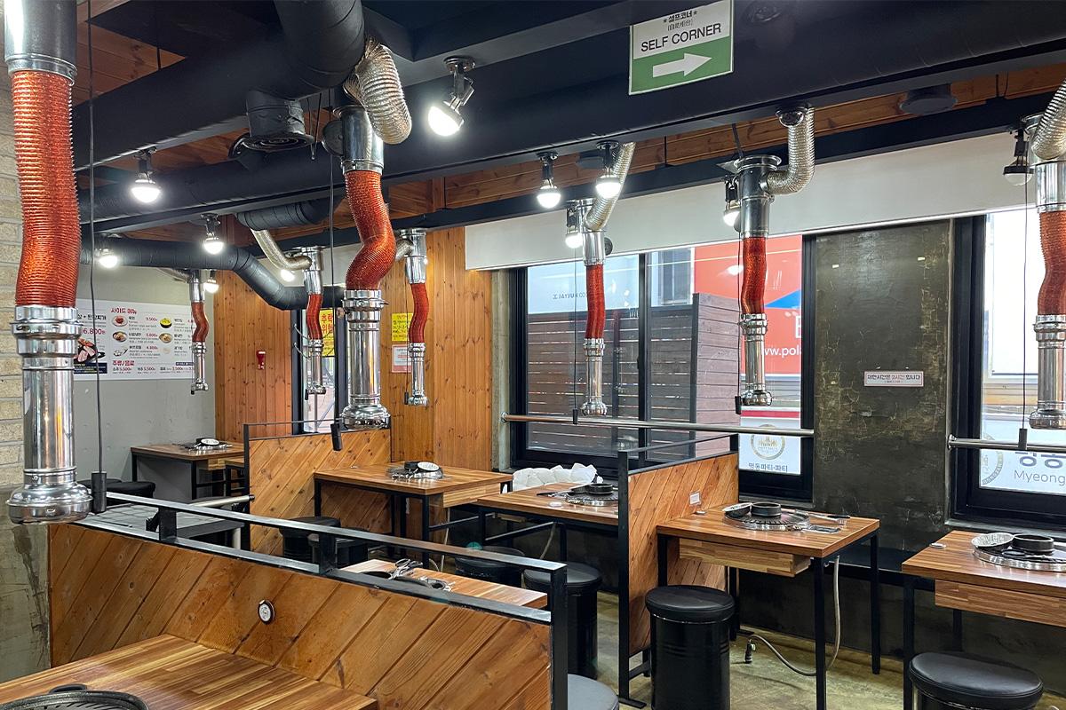 Interior of 엉터리생고기 명동점 restaurant with hardwood flooring, varnished plywood tables, and wood beam ceiling in Korea.