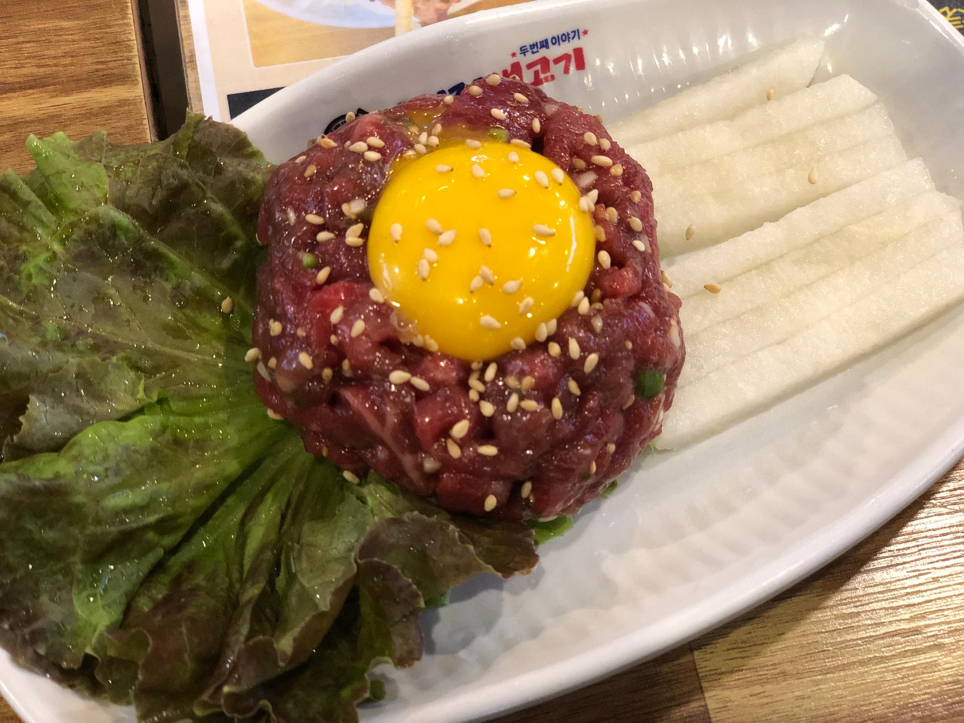 Plate of Korean steak tartare topped with egg yolk and fines herbes, served with tableware and produce at 엉터리생고기 홍대점.