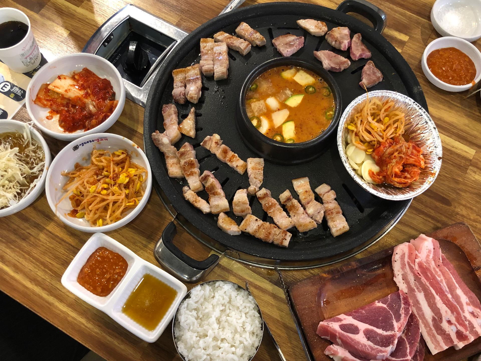 Plate of sizzling 삼겹살 (pork belly) and other dishes on the table at 엉터리생고기 홍대점 in Korea.