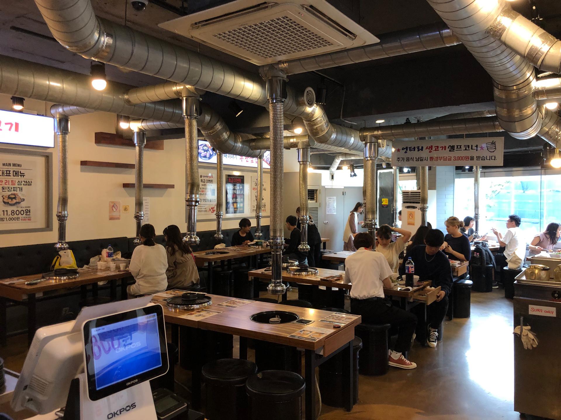 Interior of 엉터리생고기 홍대점 with tables, chairs, desks, computers, and automotive-themed decor.